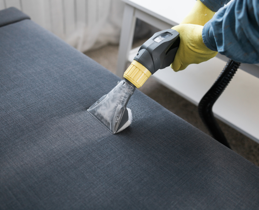 Man in protective rubber glove cleaning sofa with professionally extraction method with washing vacuum cleaner. Early spring regular cleanup. Commercial cleaning company concept